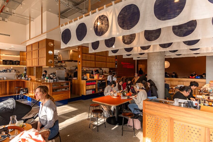 Cafe intereior with large industrial-style seating area with tables and booths, Japanese-style flags and shelving.