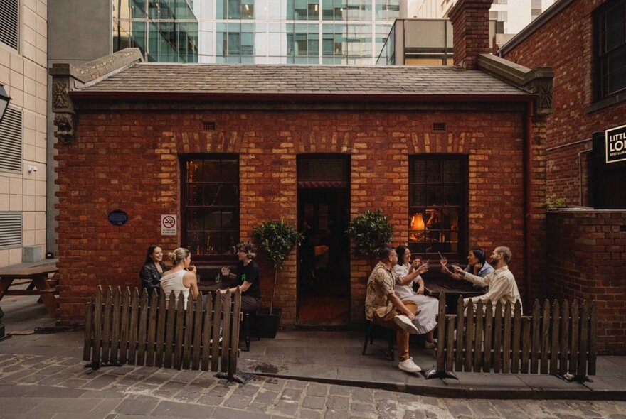 A small red brick heritage building in a Melbourne city laneway, with people seated outside at tables having a drink.