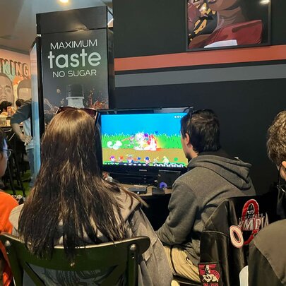 The backs of people's heads seated around gaming consoles inside a cafe or bar.