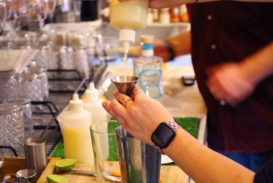 Hands preparing a drink with bottles of ingredients and glasses.