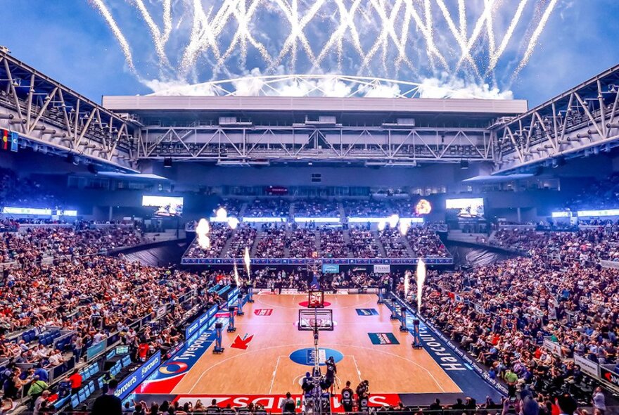 The basketball court at John Cain Arena filled with fans in the seats and with an open roof, showing the night sky.