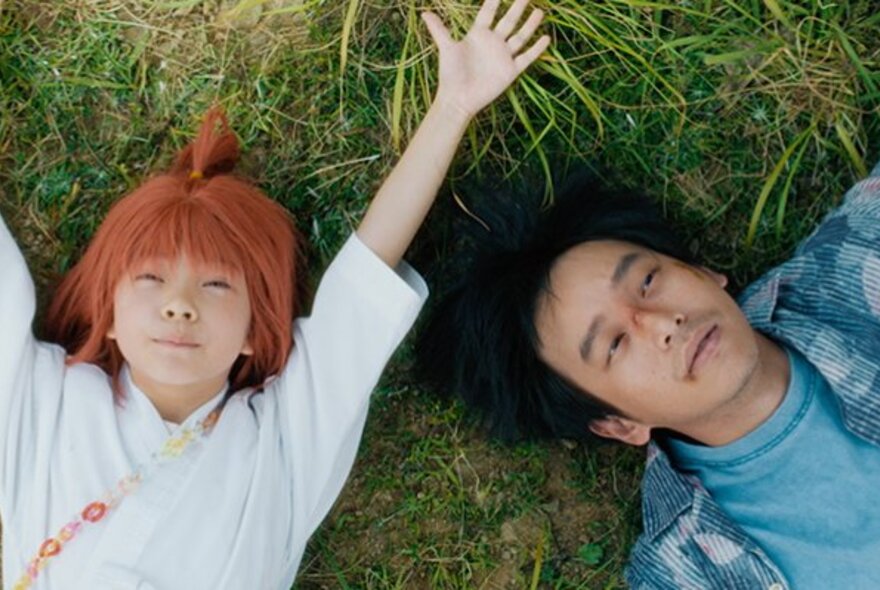 Still from a film of two young adults lying on the grass on their backs staring up into space.