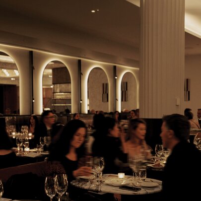 Diners at Dolly European Restaurant and Bar, with backlit arched mirrors on the wall and a central column surrounded by tables.