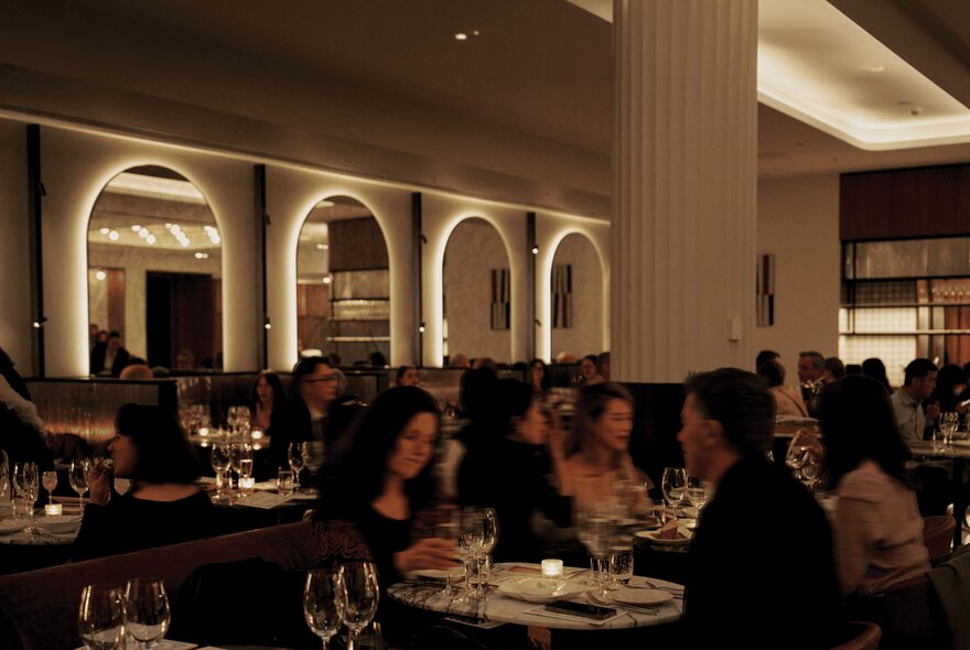 Diners at Dolly European Restaurant and Bar, with backlit arched mirrors on the wall and a central column surrounded by tables.