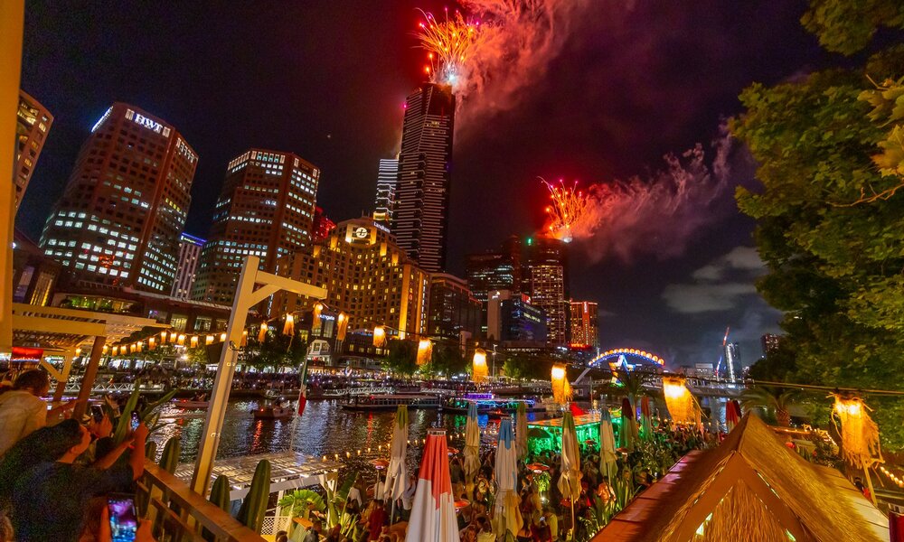 Red fireworks over the city viewed from a floating bar with umbrellas and lanterns.