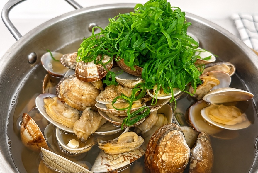 A steel bowl of steamed clams with a spring onion garnish. 