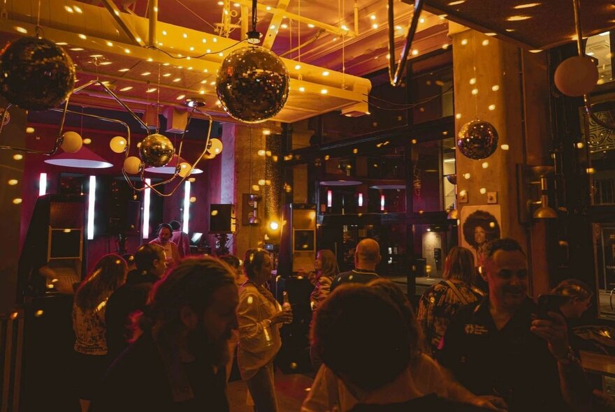 The inside of a dimly lit venue with patrons dancing underneath disco balls.