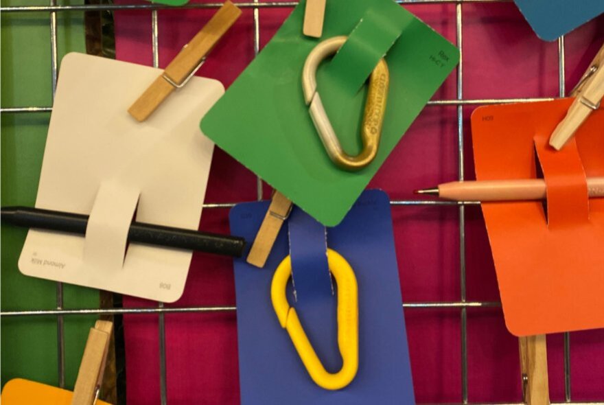 Tags of varying colours featuring carabiners clipped onto wire mesh with wooden pegs. 