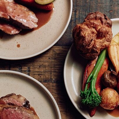 Looking down at three plates of roast meats with Yorkshire pudding, roast potatoes, vegetables and gravy.
