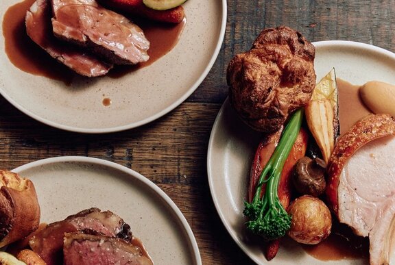Looking down at three plates of roast meats with Yorkshire pudding, roast potatoes, vegetables and gravy.