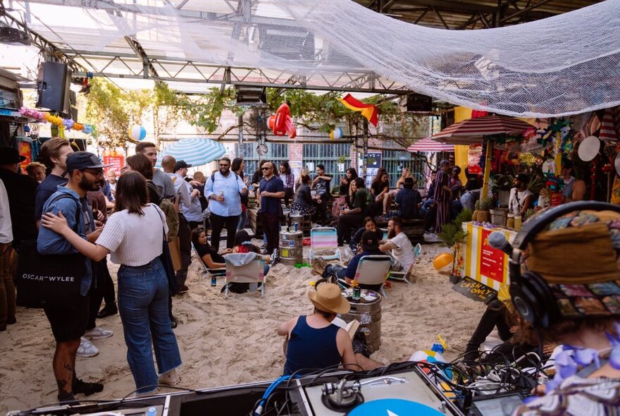 The Section 8 outdoor bar with sand covering the floor, beach umbrellas and people gathered around socialising and drinking.