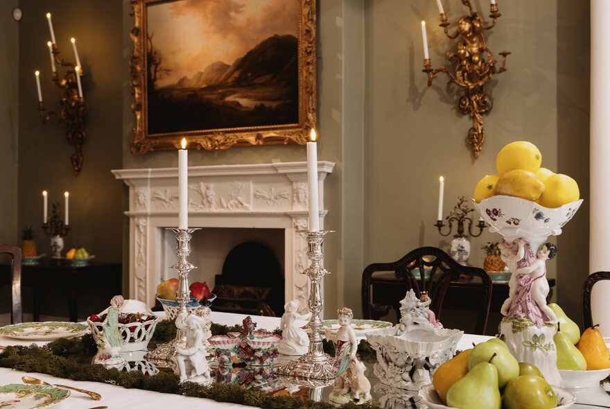 Grand dining room with fireplace, painting, candelabras and set table.