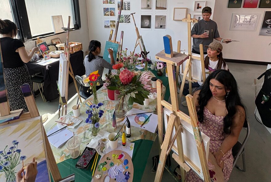 A group of people painting at easels in a studio space.