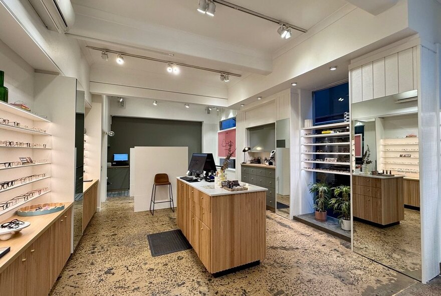 The interior of an eyeglass store, with shelves of eyeglasses along the side walls and a central service counter.