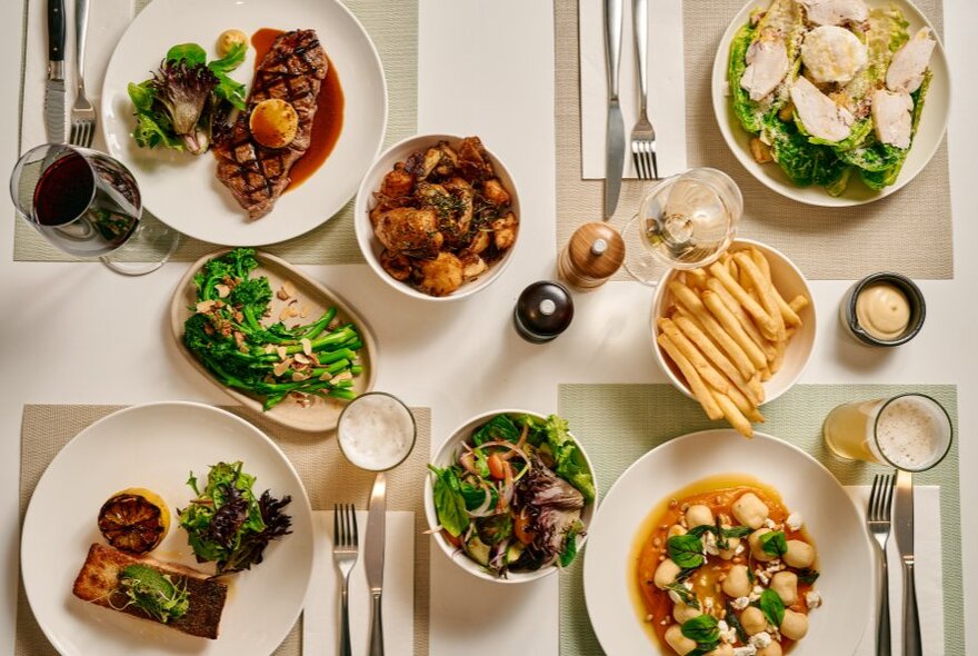 Four meals laid out in place settings at a table, seen from above alongside cutlery and share plates.