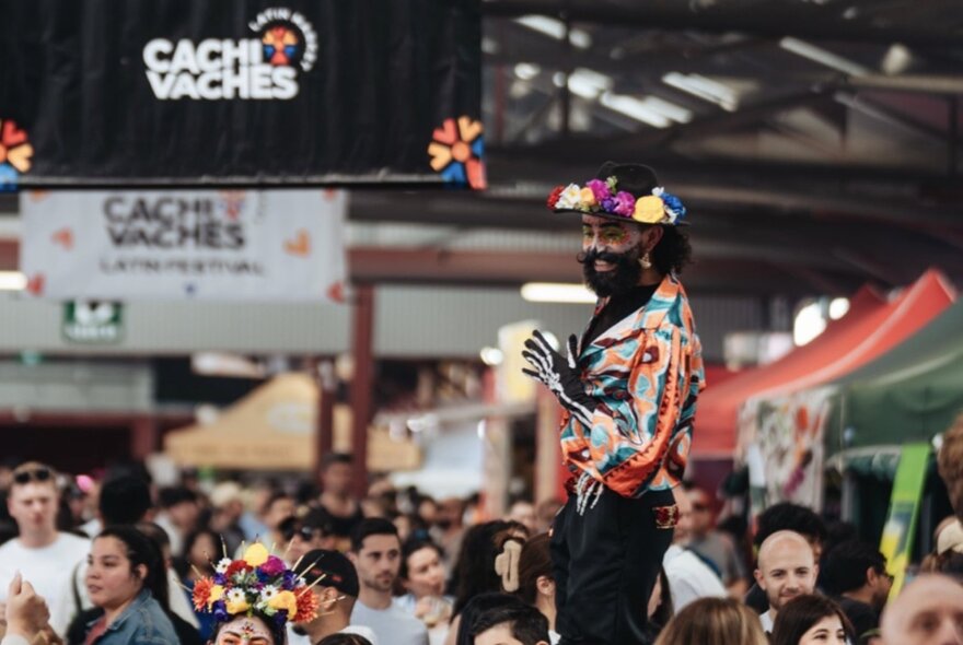 Performer on stilts in a Queen Victoria Market shed with people looking on.