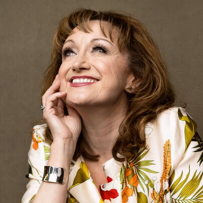 Portrait of Australian theatrical legend Caroline O’Connor AM, smiling while looking up with her hand on her cheek.