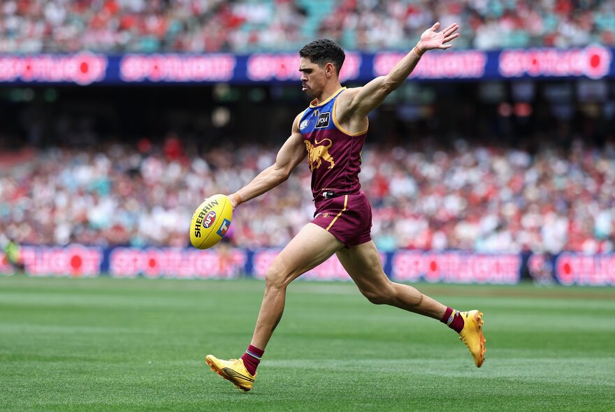 A Brisbane Lions player about to kick a football in front of a packed crowd.