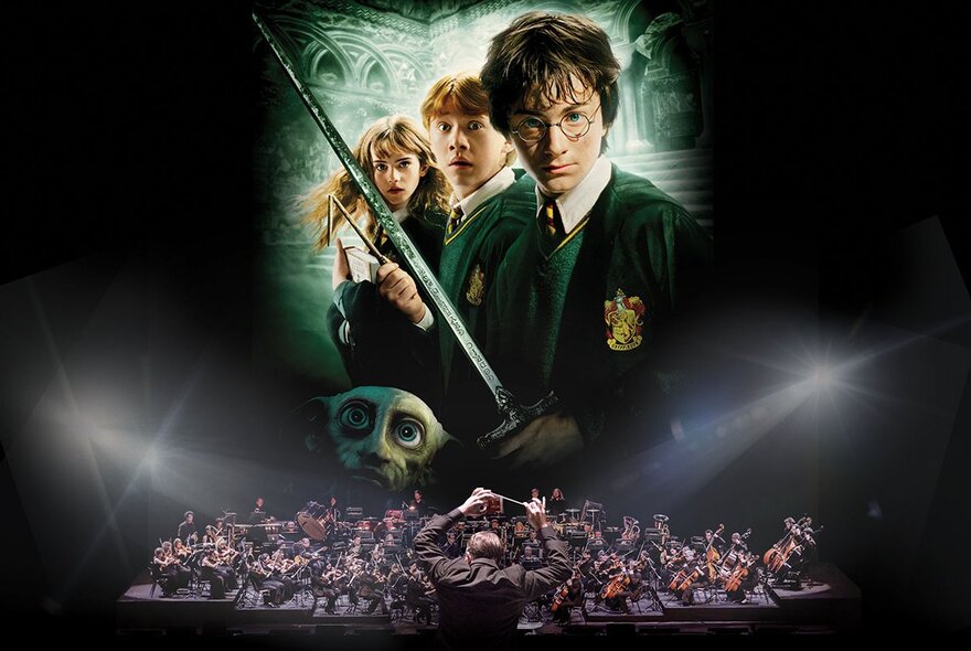 A movie still from the film Harry Potter and the Chamber of Secrets on a large screen at Hamer Hall, while an orchestra play the live score seated on the stage underneath the film screening.