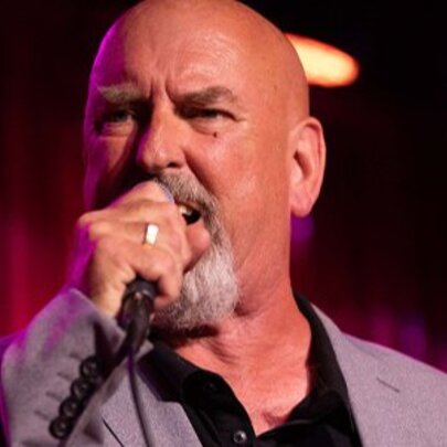 Bald singer performing with microphone, wearing a grey suit.