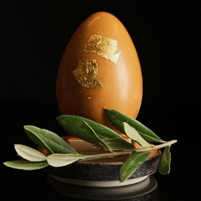 A large caramel chocolate egg with 24 karat gold leaf, resting on a small platter with a sprig of a native Australian bush.