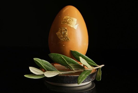 A large caramel chocolate egg with 24 karat gold leaf, resting on a small platter with a sprig of a native Australian bush.