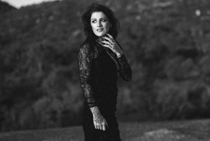 Woman wearing black lace dress, standing in front of dark landscape.