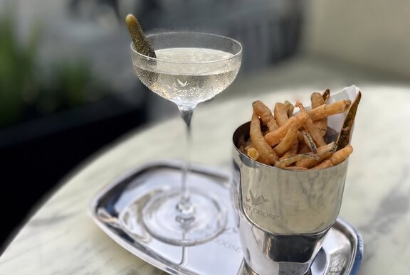 A classic martini paired with a side of crispy fried pickles on a silver tray on a marble-topped table.