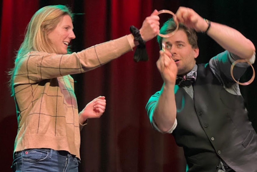 A magician demonstrates a trick with a ring a woman is holding on stage