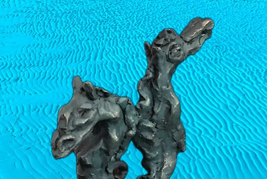 An abstract, dark sculpture resembling two seahorses against a bright blue background with wavy lines.