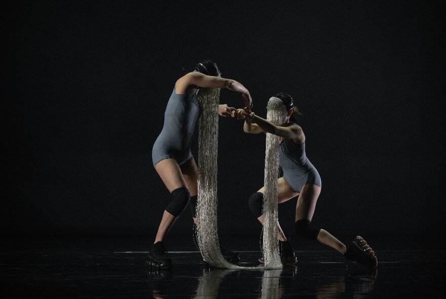 Two members of dance group Neon Dance performing on a darkened stage, their faces joined by many fine threads. 