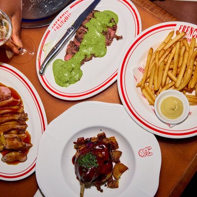 A restaurant table set with steak and green sauce, fries, wine and more.