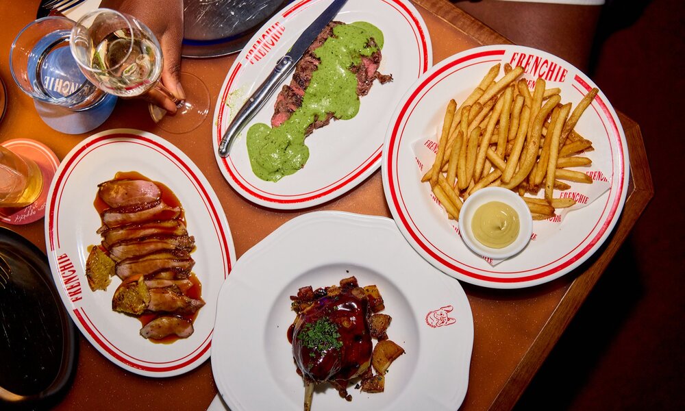 A restaurant table set with steak and green sauce, fries, wine and more.