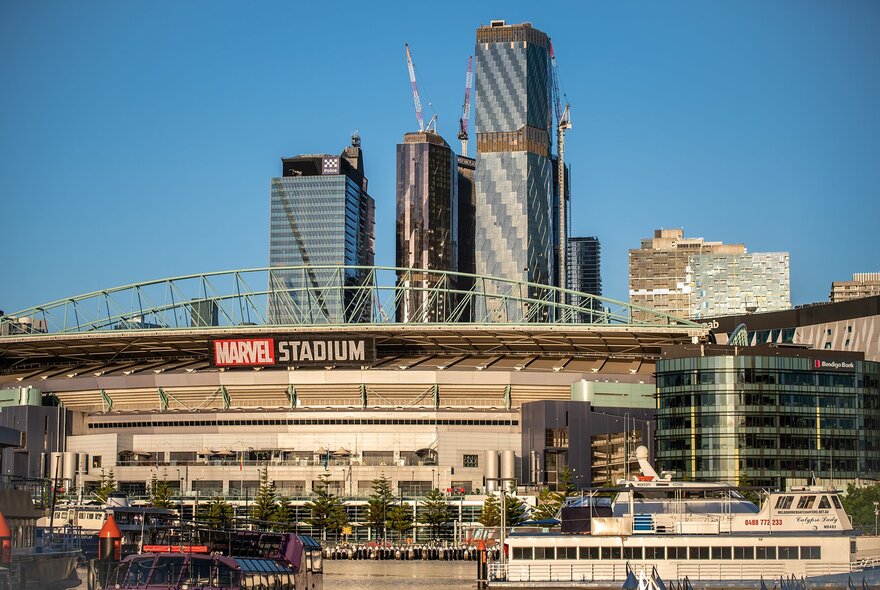 A waterside football stadium with a sign reading Marvel Stadium on a sunny day in the city.