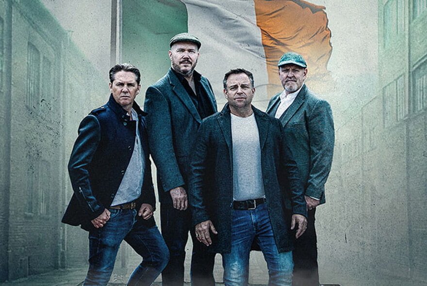 Four members of the Irish folk band The High Kings posing in a serious way with a backdrop of an Irish flag. 