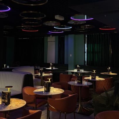 Dimly lit bar venue with spotlit tables, couches and overhead neon rings.