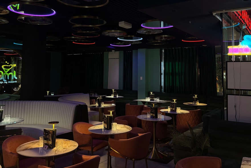 Dimly lit bar venue with spotlit tables, couches and overhead neon rings.