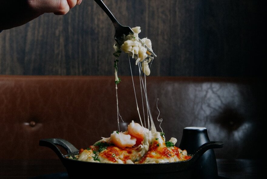 A fork pulling away from a bowl of food with strings of cheese visible. 