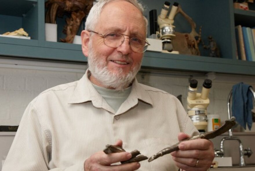 A bearded man holding archaeological fragments in a science laboratory.