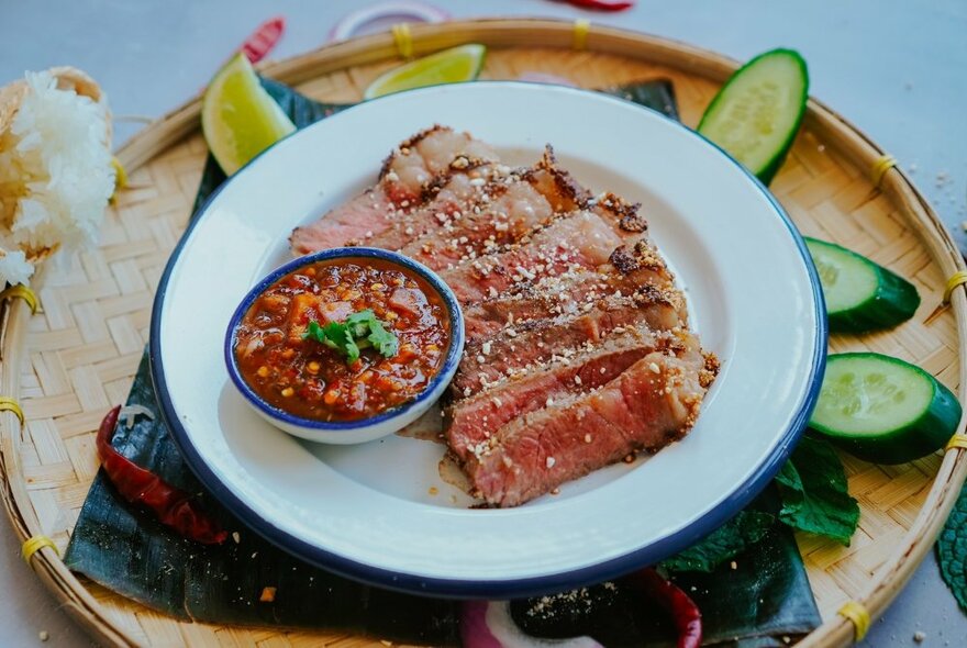 A plate with small rolls and dipping sauce with cucumber around the plate underneath. 