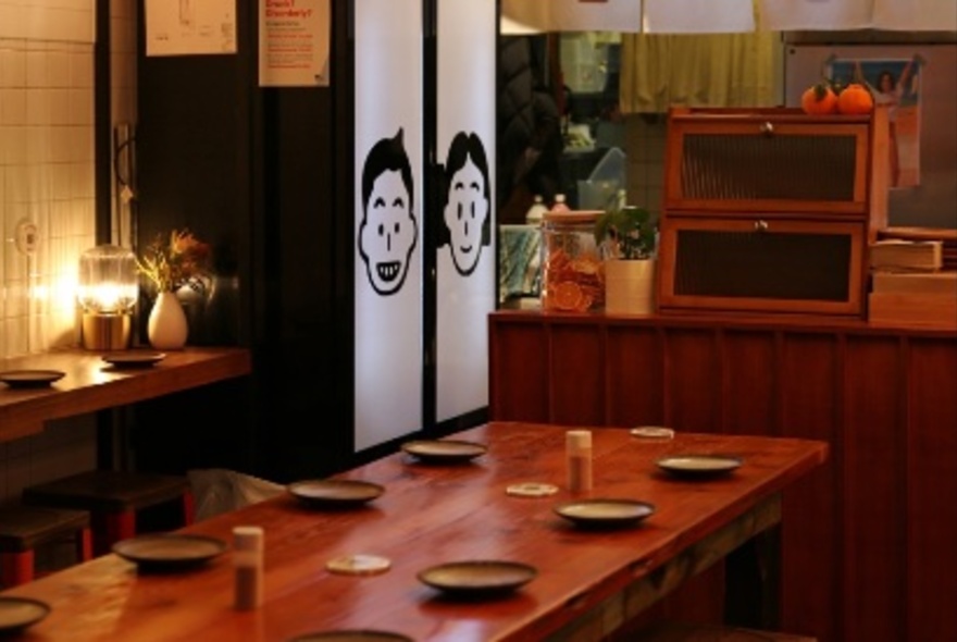 Interior of a cafe with a long table set with plates, a soft light on a side wall counter and fabric wall hangings.