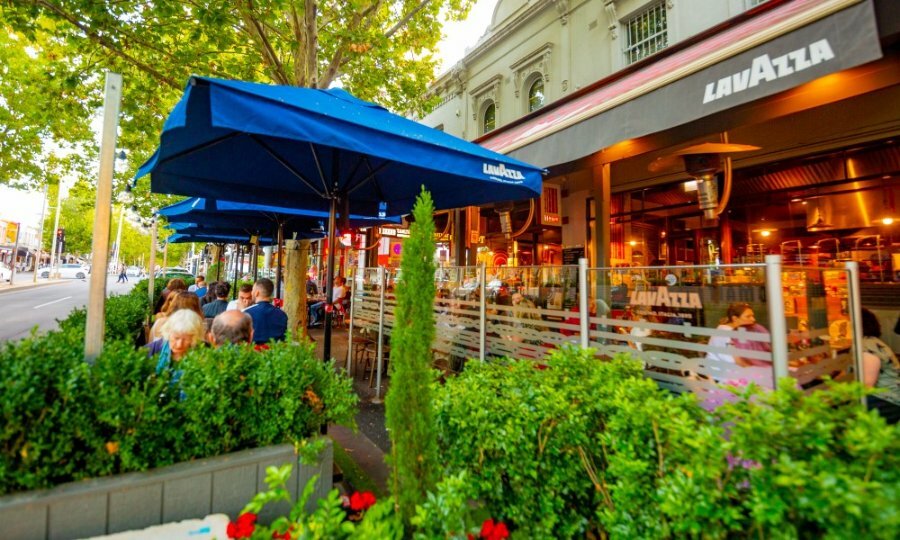 People dining outside a restaurant surrounded by greenery.