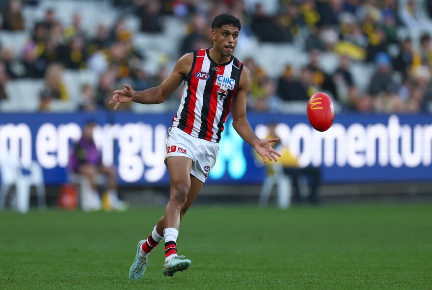 A St Kilda football player kicks a red Sherrin football during a match. 
