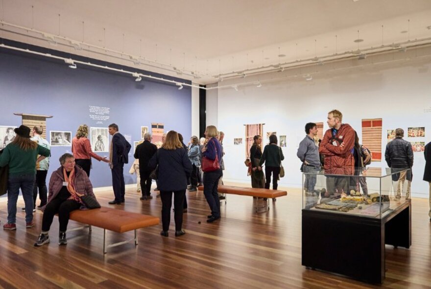 People walking around a gallery room, looking at artworks on the wall or in display cabinets.