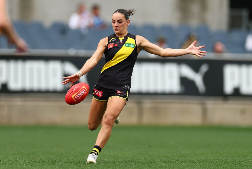 A Richmond Tigers ALFW player kicking a red football during a game.