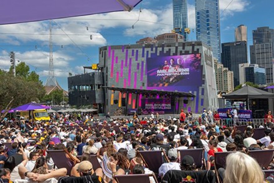 People crowded around the Big Screen at Fed Square on a sunny day.
