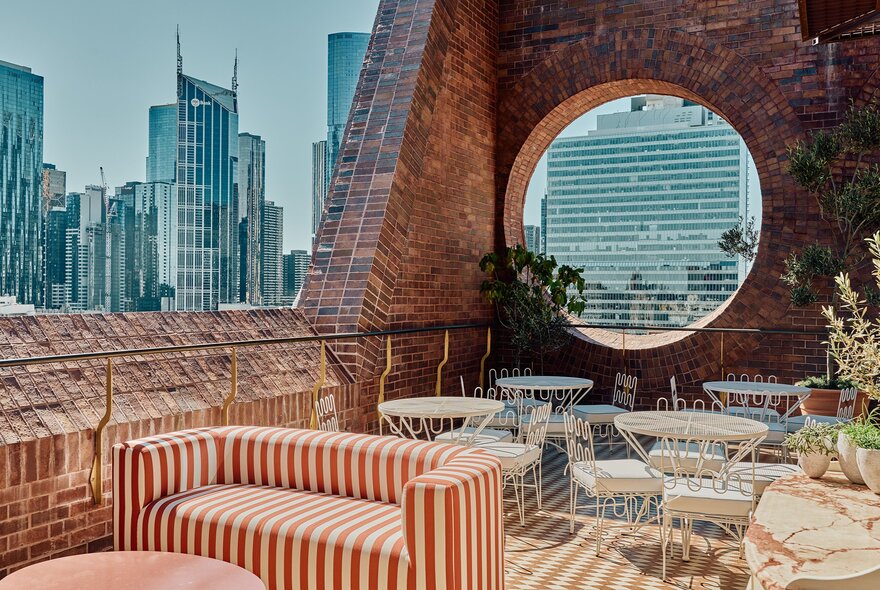 An open rooftop bar during the day with striped sofas and a large round window.