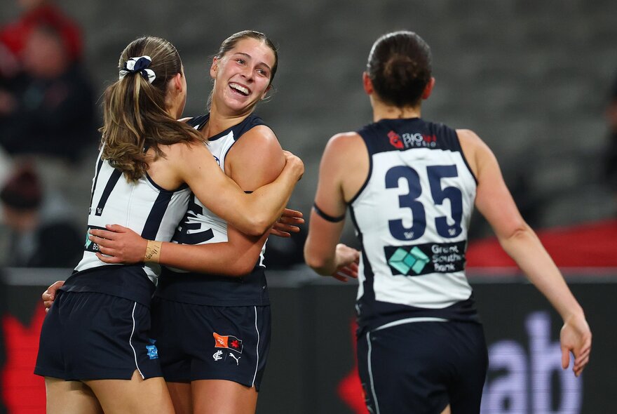 Three Carlton AFLW players celebrating on the field. 