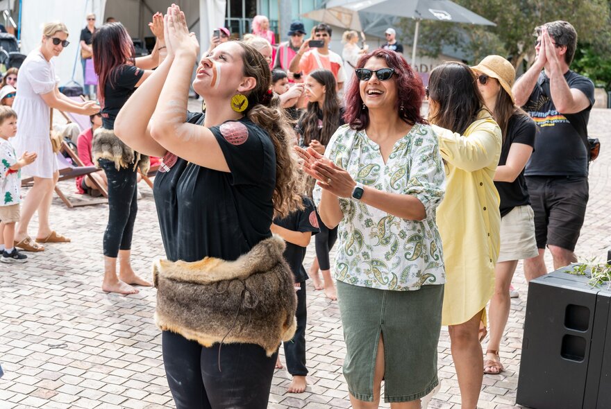 People outside at Fed Square enjoying the festivities at Koorie Krismas, partaking in a dance.