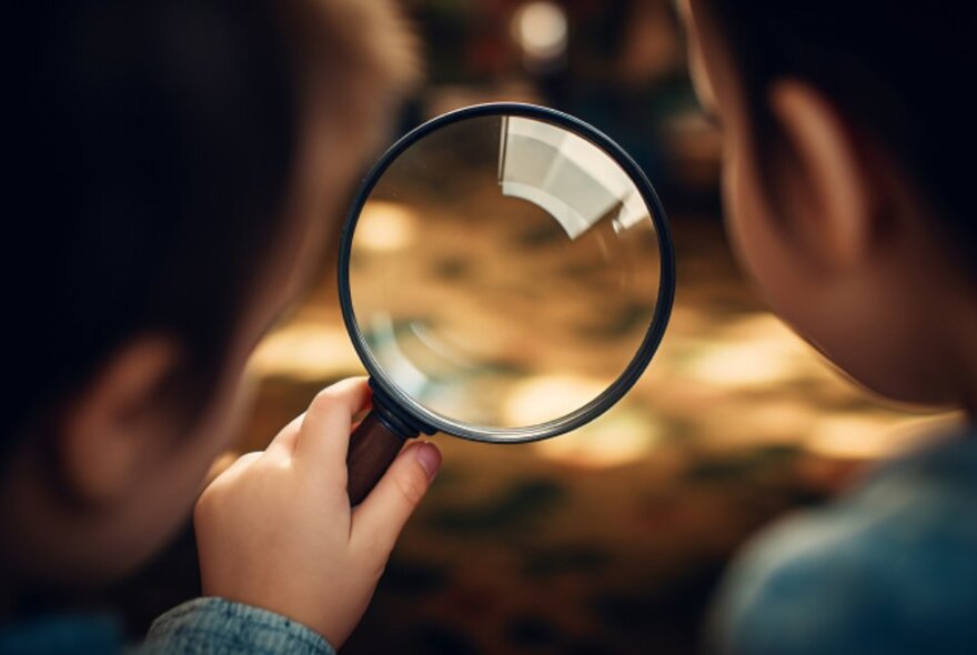 Close up of two kids looking though a magnifying glass.